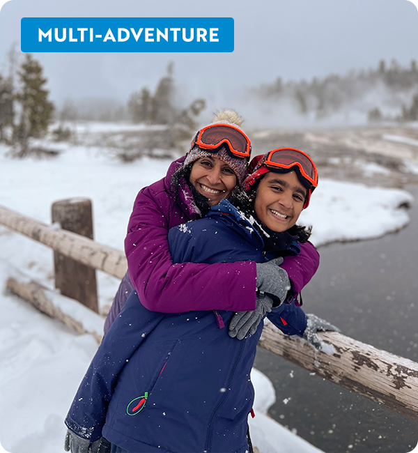 A woman hugging a child from behind standing in the snow, smiling at the camera