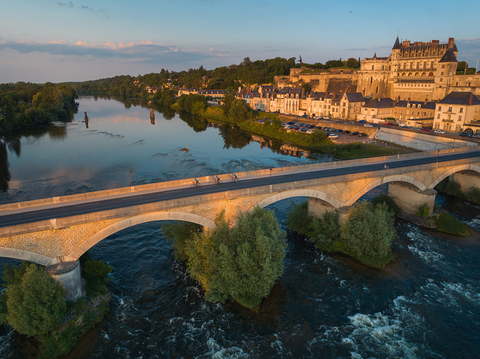 Bird's eye shot of cyclists over Loire River during sunset.  Ch&acirc;teau Royal d'Amboise behind.
