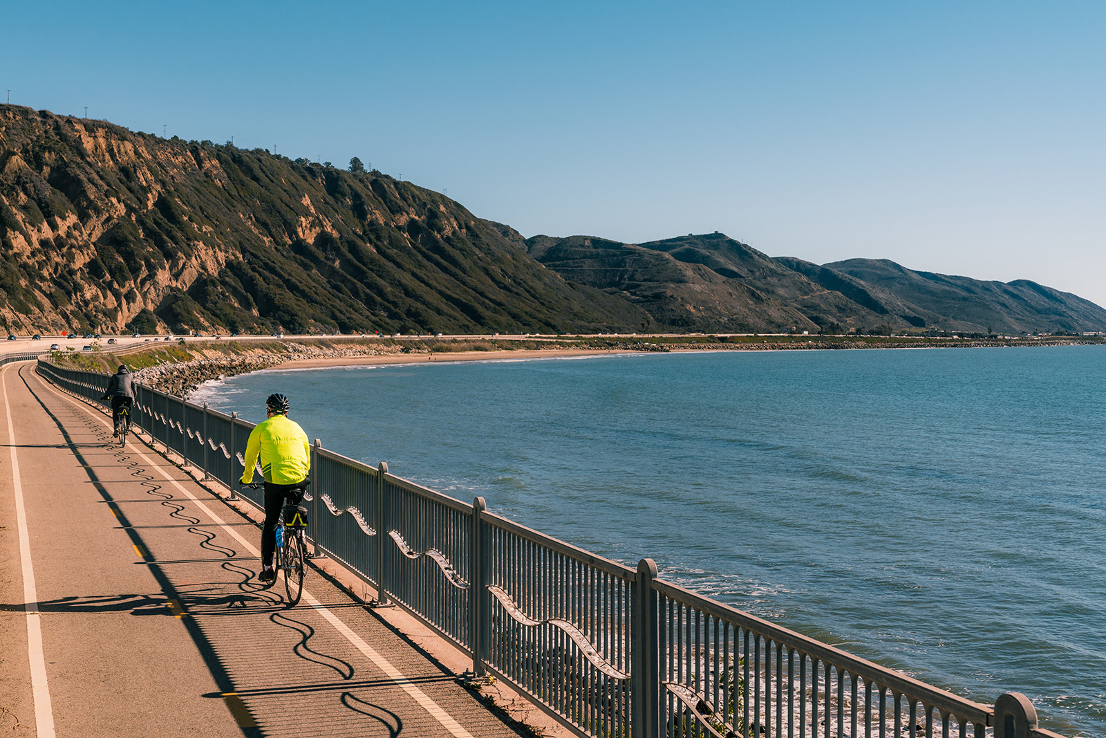 People biking along coastal road, ocean beside them.
