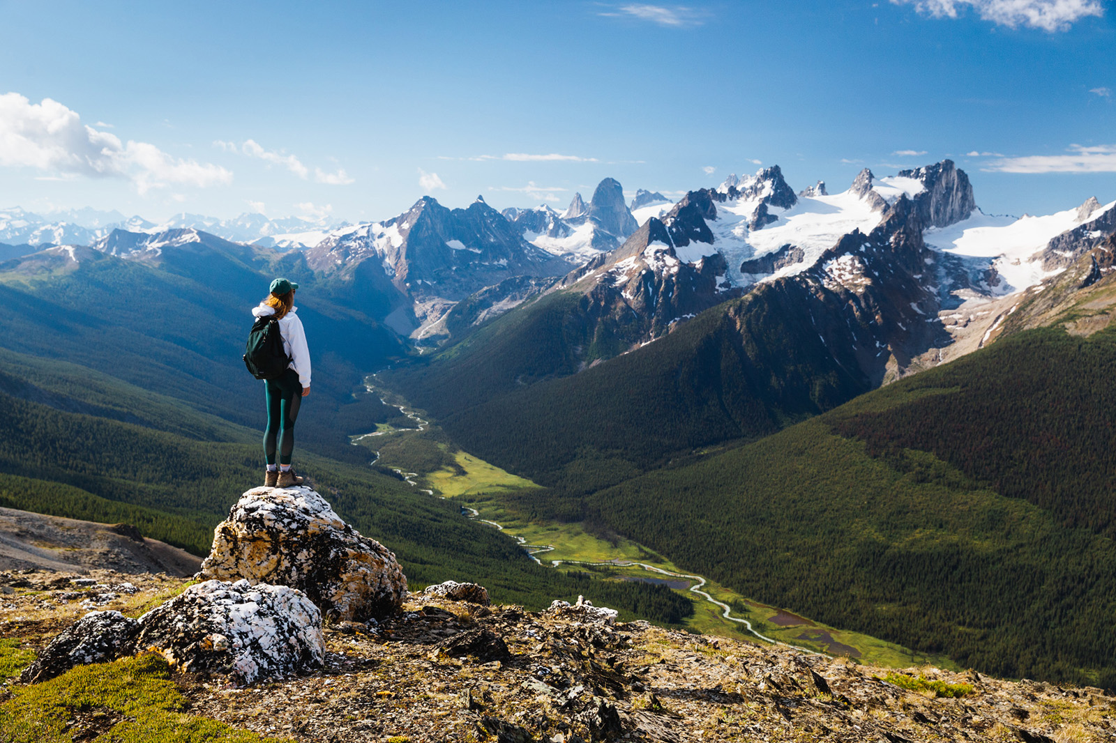Guest standing on rocky hilltop, looking towards larger mountains.