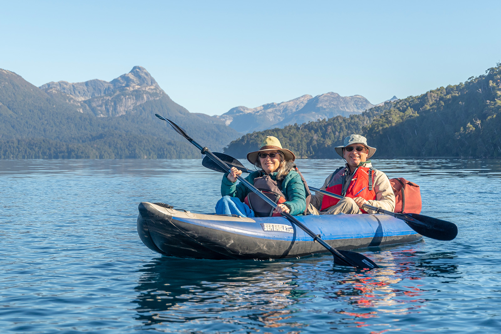 Two guests kayaking, sharp mountains in distance.
