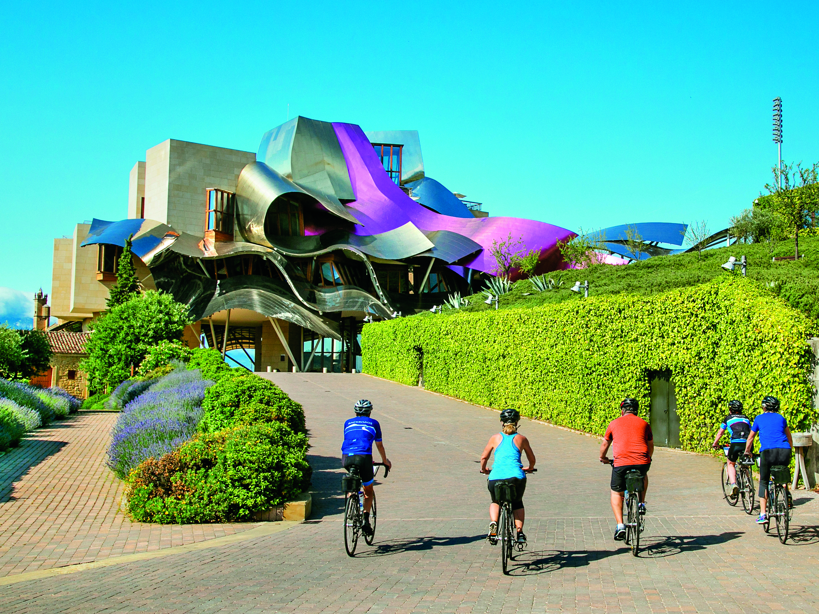 Four bikers riding towards modern building in Basque Country.