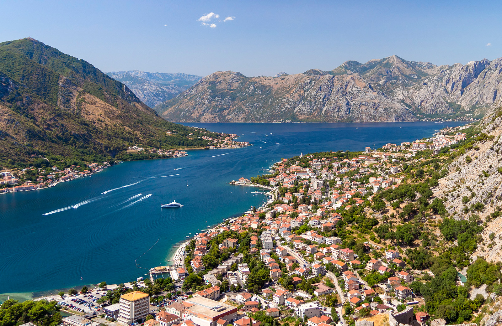 Bird's eye of Croatian riverside city, mountains all around, boats in river.