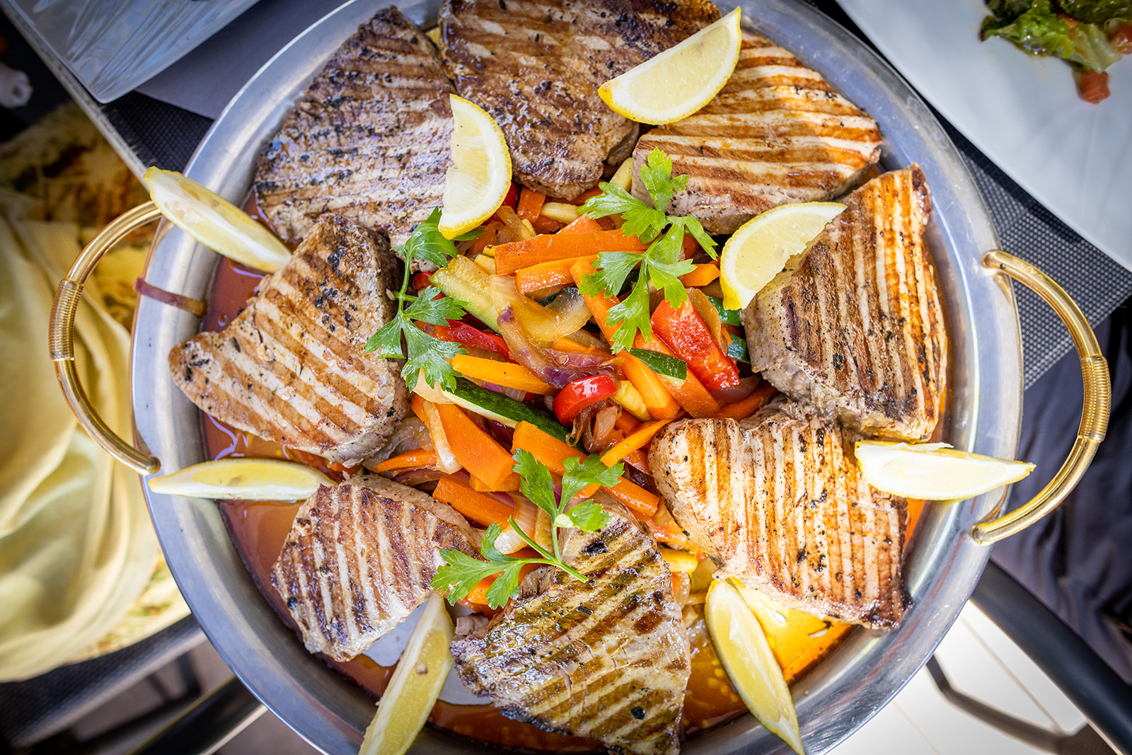 Platter of food, grilled meat, veggies, lemon slices, etc.
