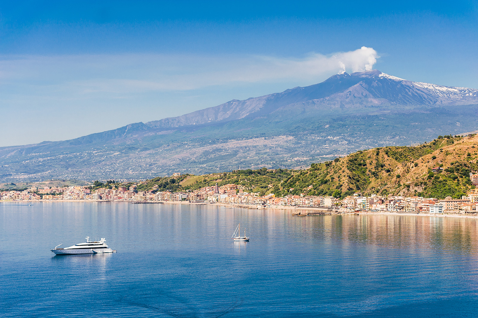 Wide shot of Mount Etna, small boats in water in foreground.