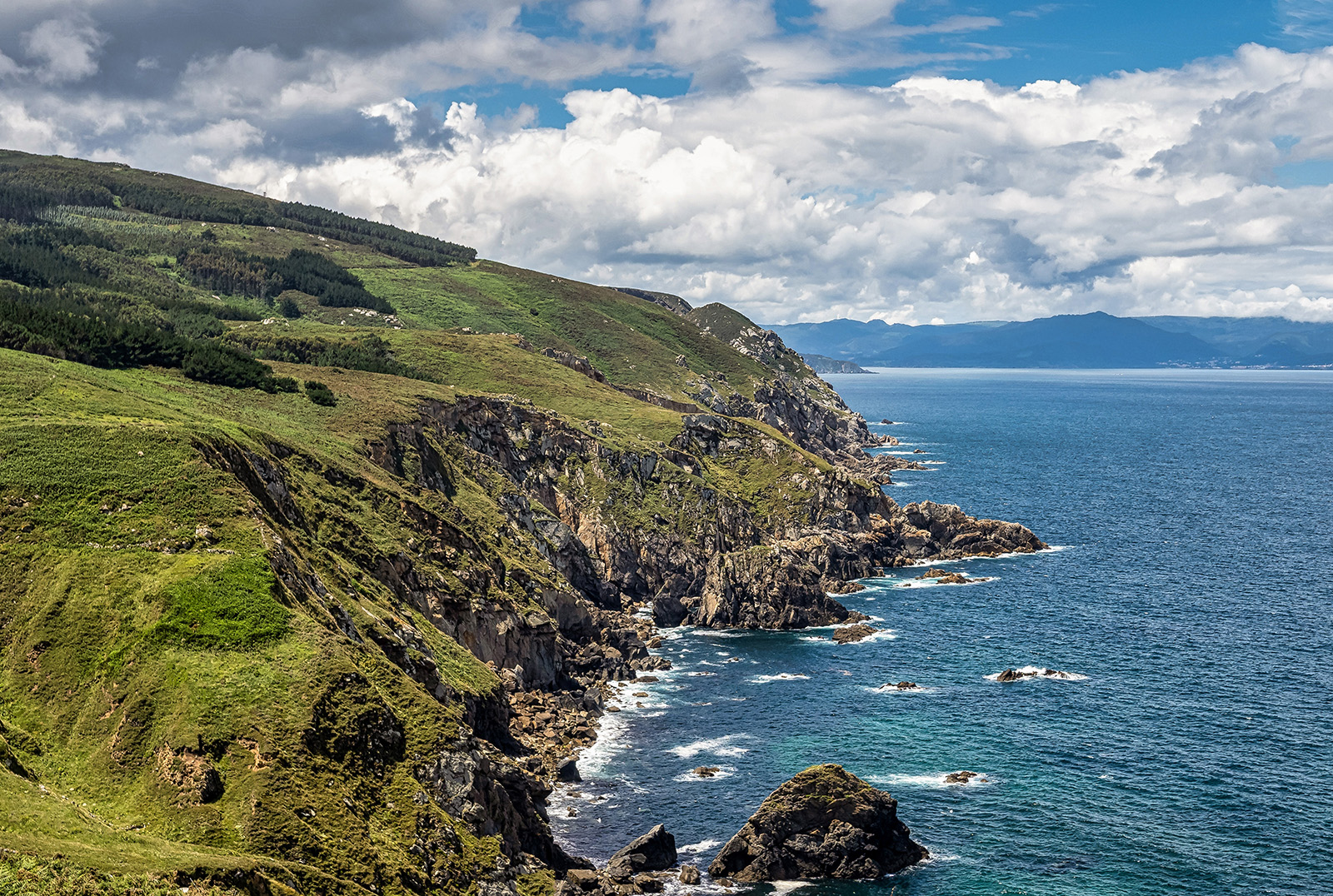 Shot of green, craggy coastline, ocean to right.