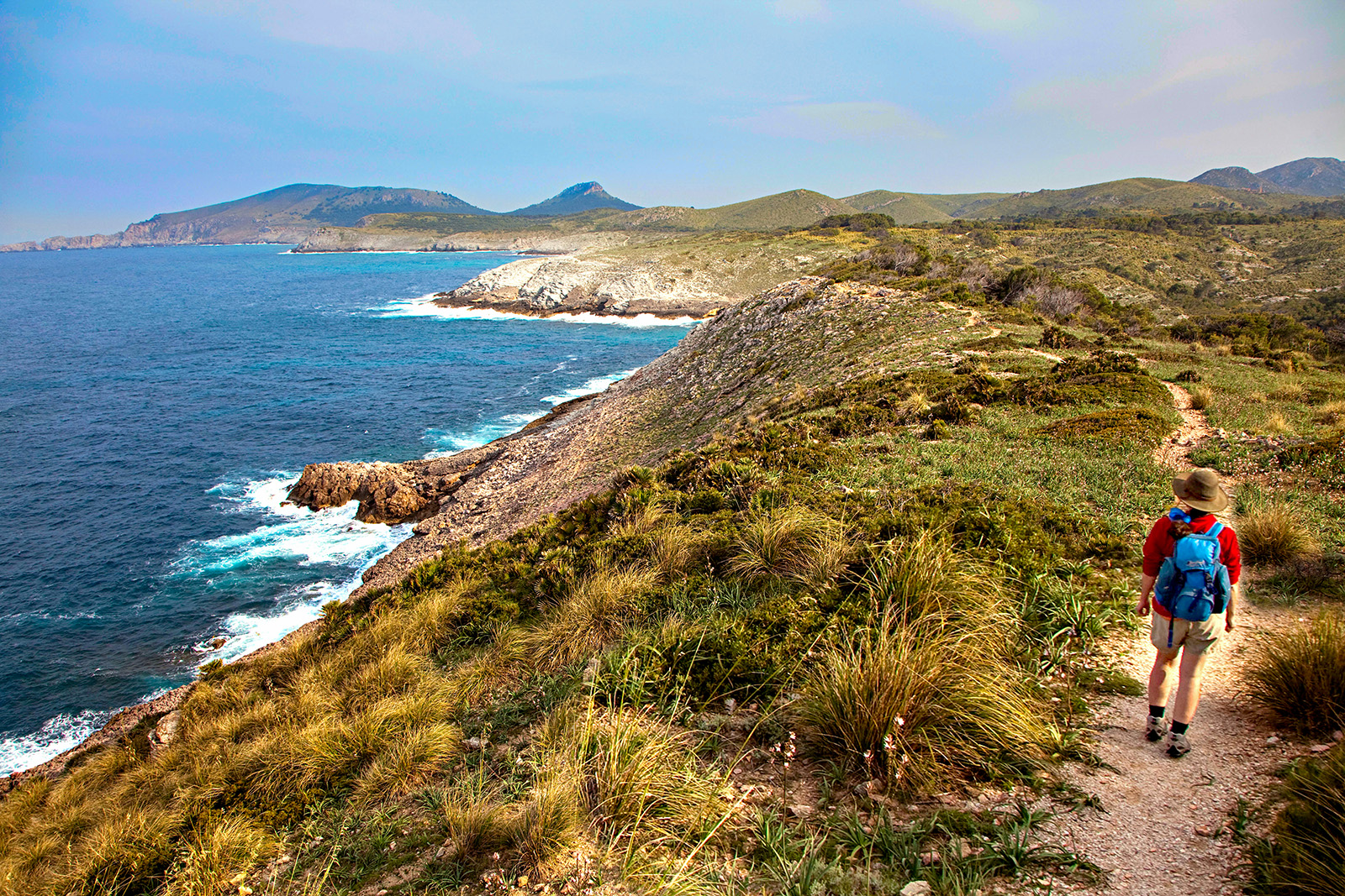 Guest walking beside ocean, towards golden hilly vista.