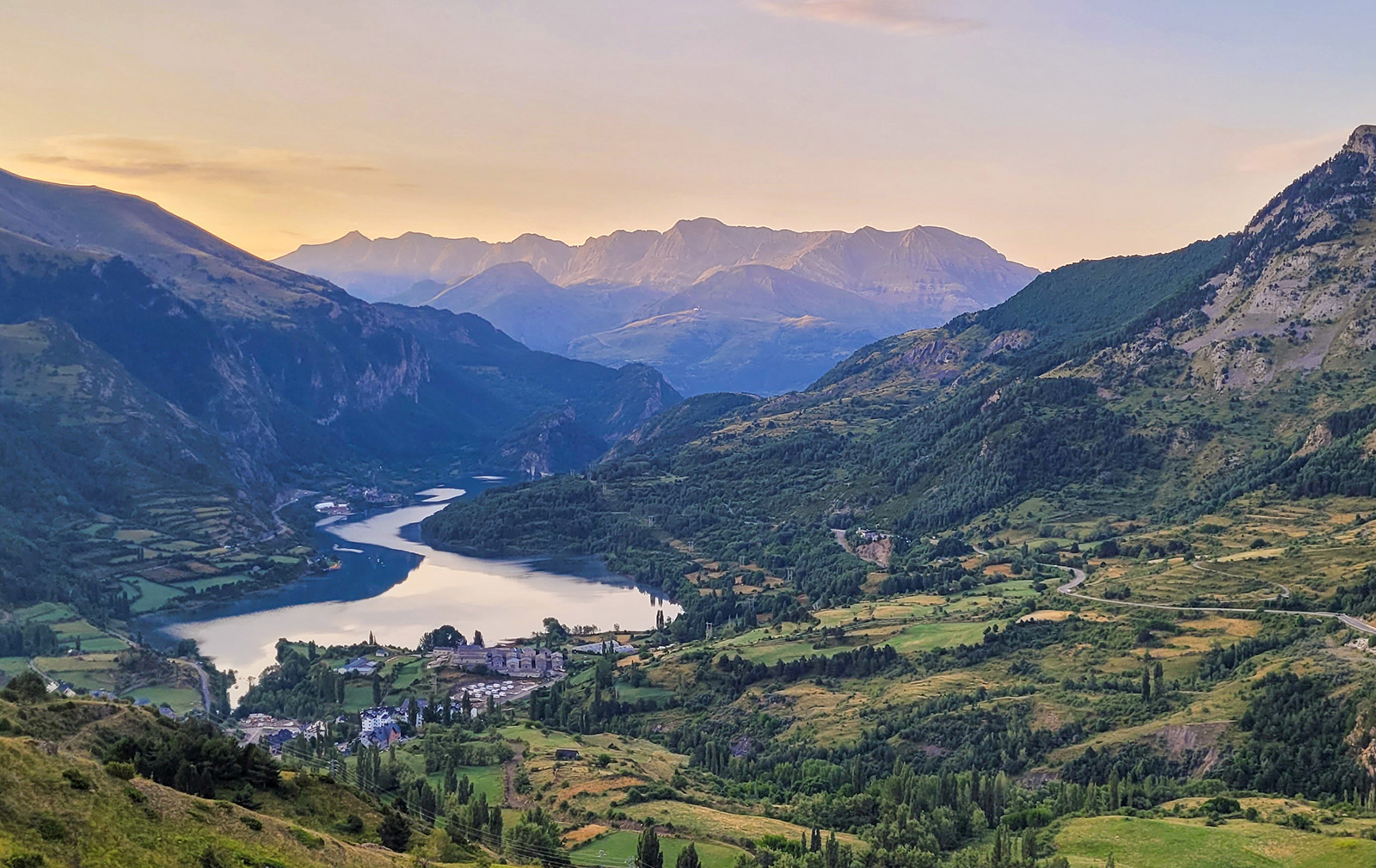 Wide shot of mountain valley town, river running through, sunset.