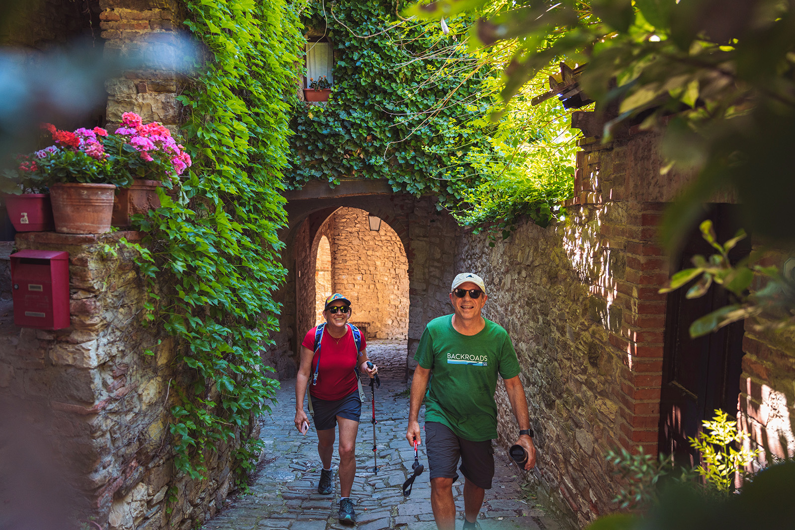 Two guests walking through arched brick walkway, flowers and hanging plants above.