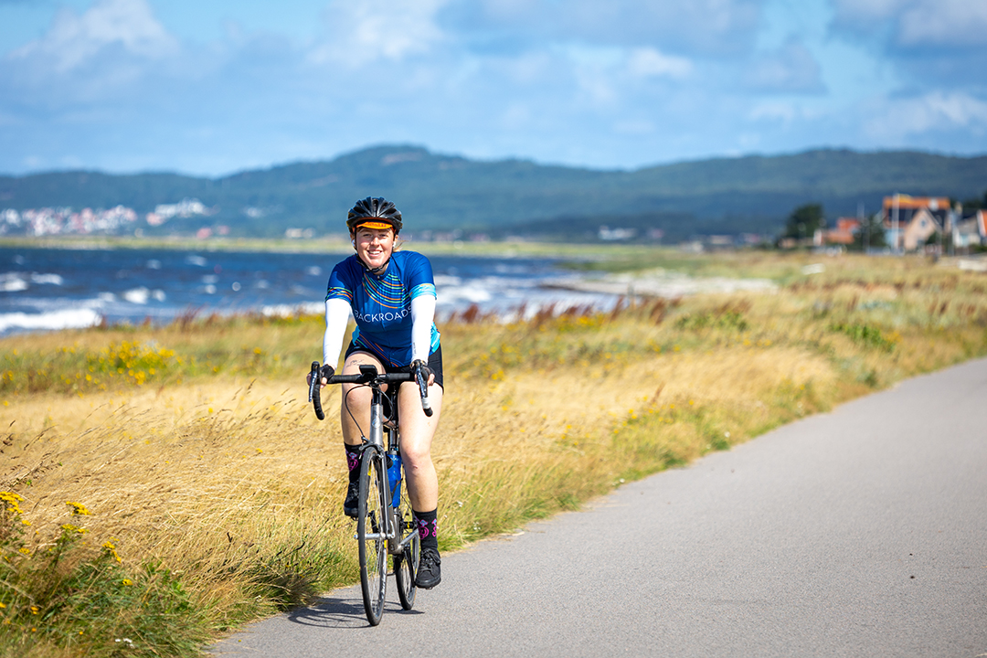Woman smiling while riding a pike on the pavement, with the ocean in the background
