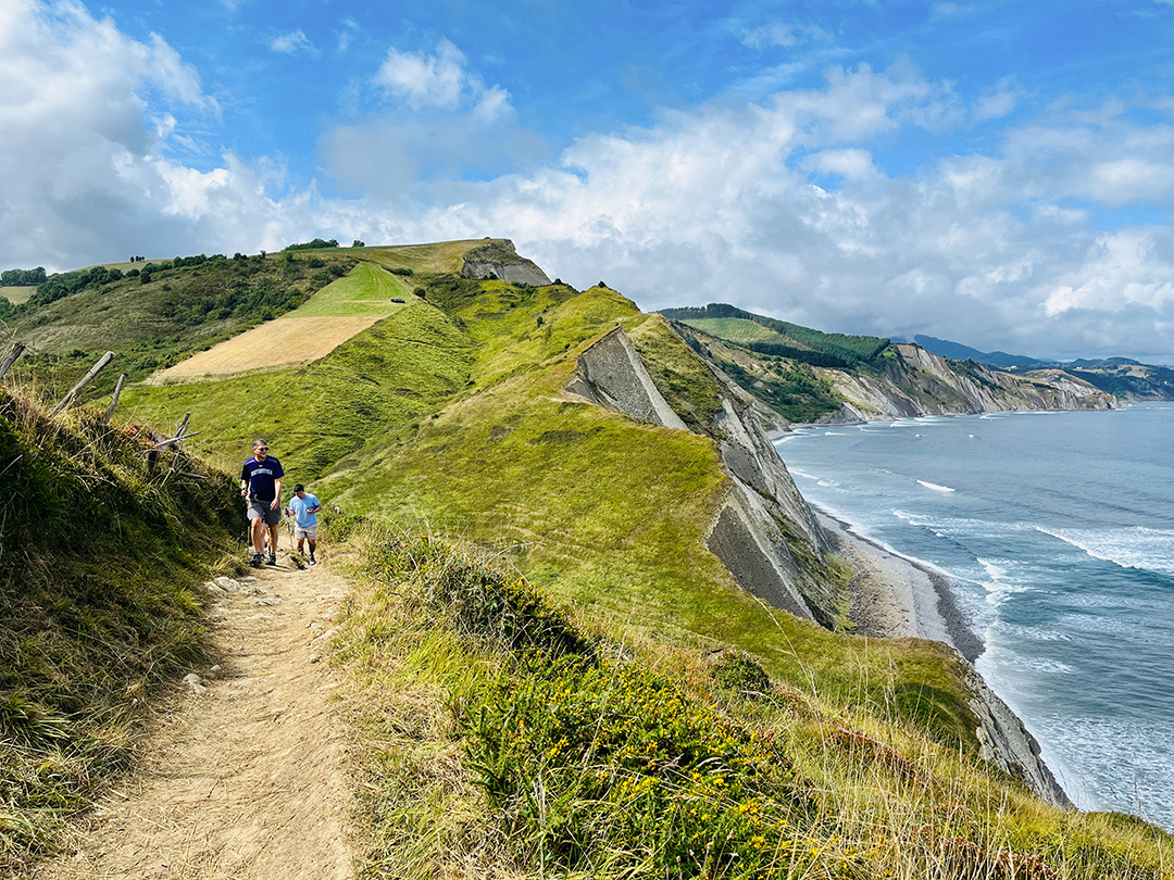Group of people hiking on a sandy trail, with cliffs and the ocean to the right