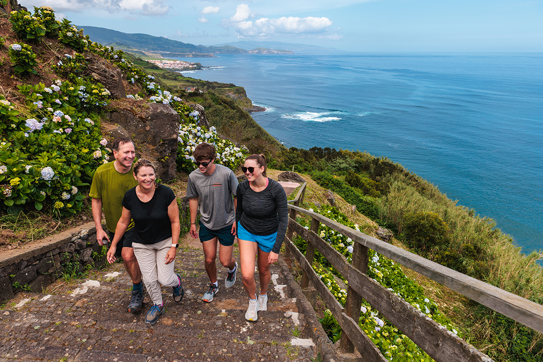 Group of people walking up stairs, with large cliffs and the ocean in the background