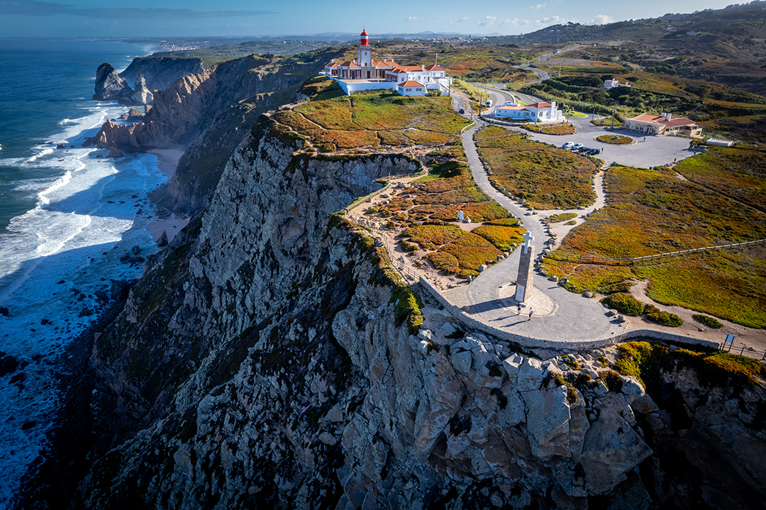 A cliff with a church, an open parking log and a sculpture with a cross in the center