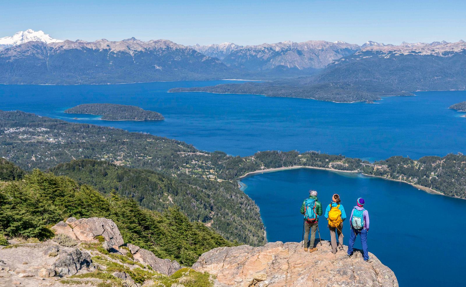 Group of 3 people standing on a cliff, looking out to a lake