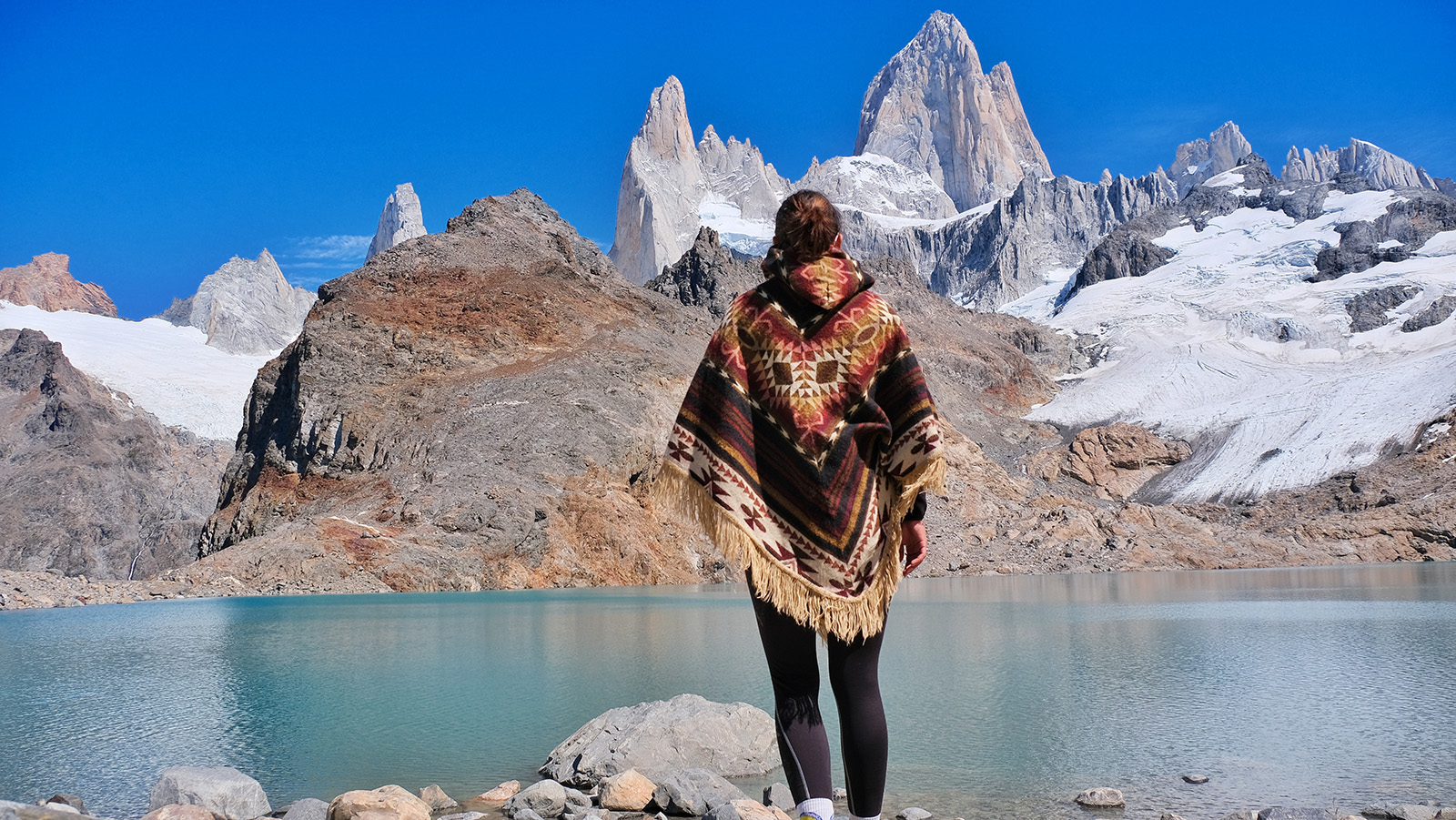 Woman wearing a poncho looking out towards a lake and mountains