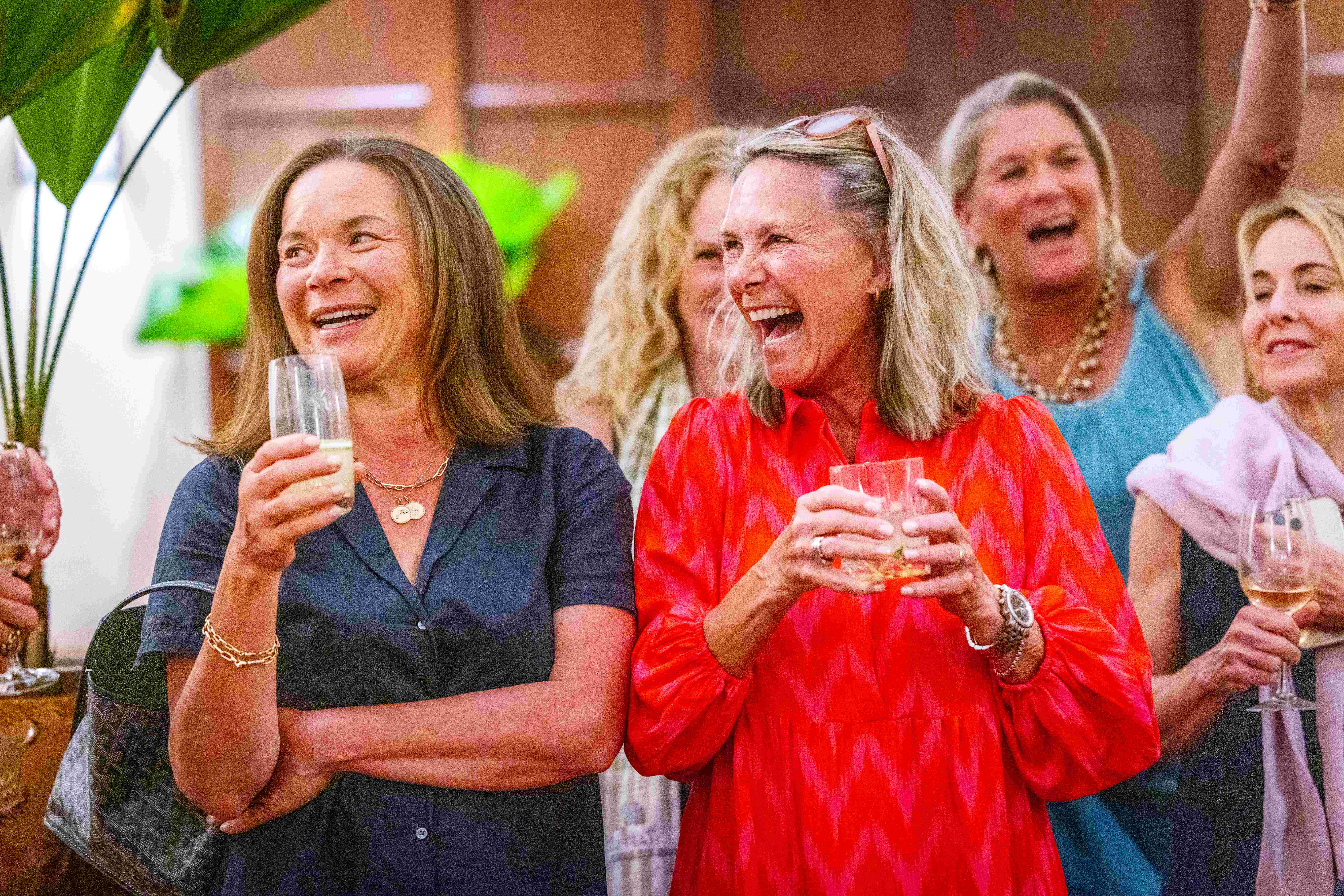 Group of women holding glasses of wine and alcohol while smiling and laughing