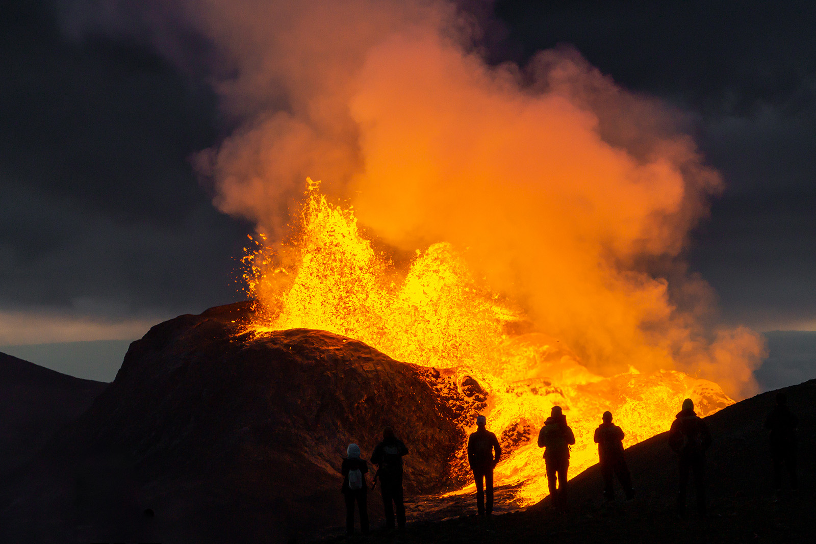 Group of people looking at an active volcano covered in smoke