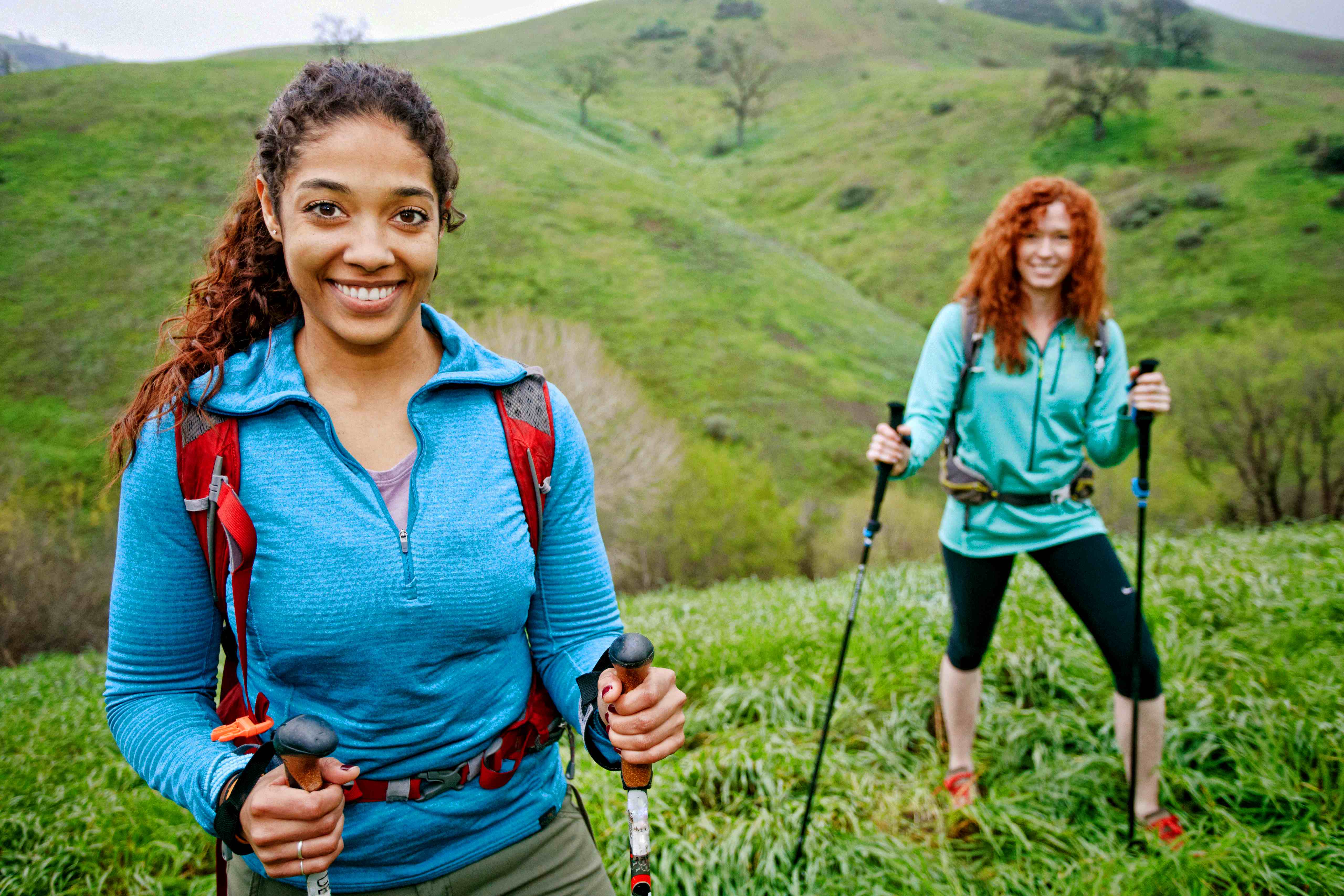 Two women with walking poles on top of a grassy hill