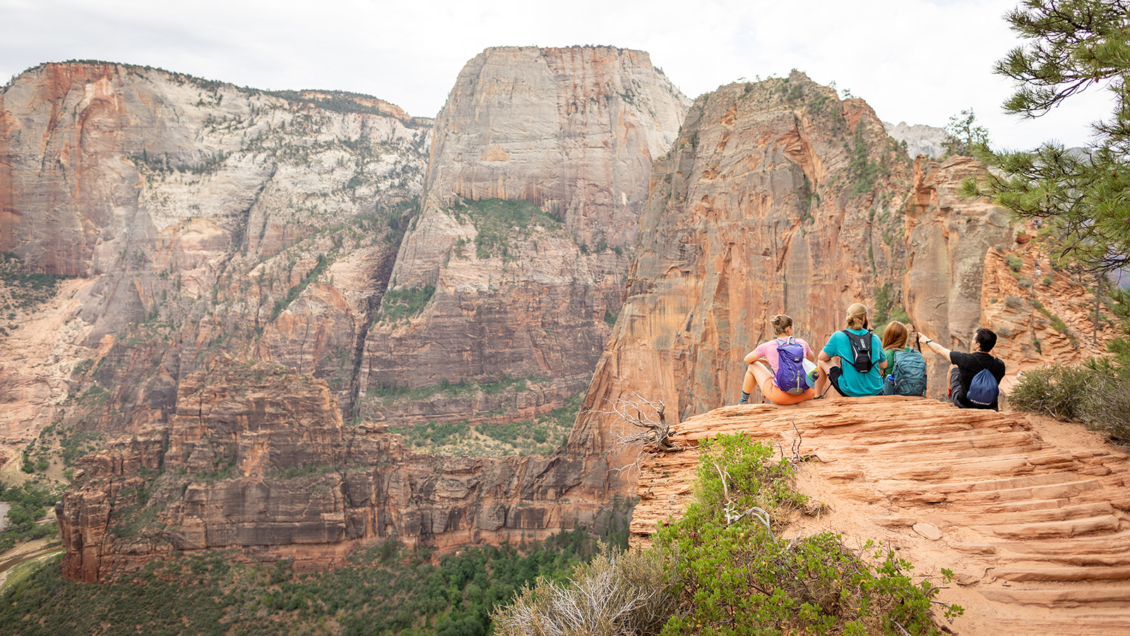 Three women and 1 man sitting on cliff looking at larger mountains