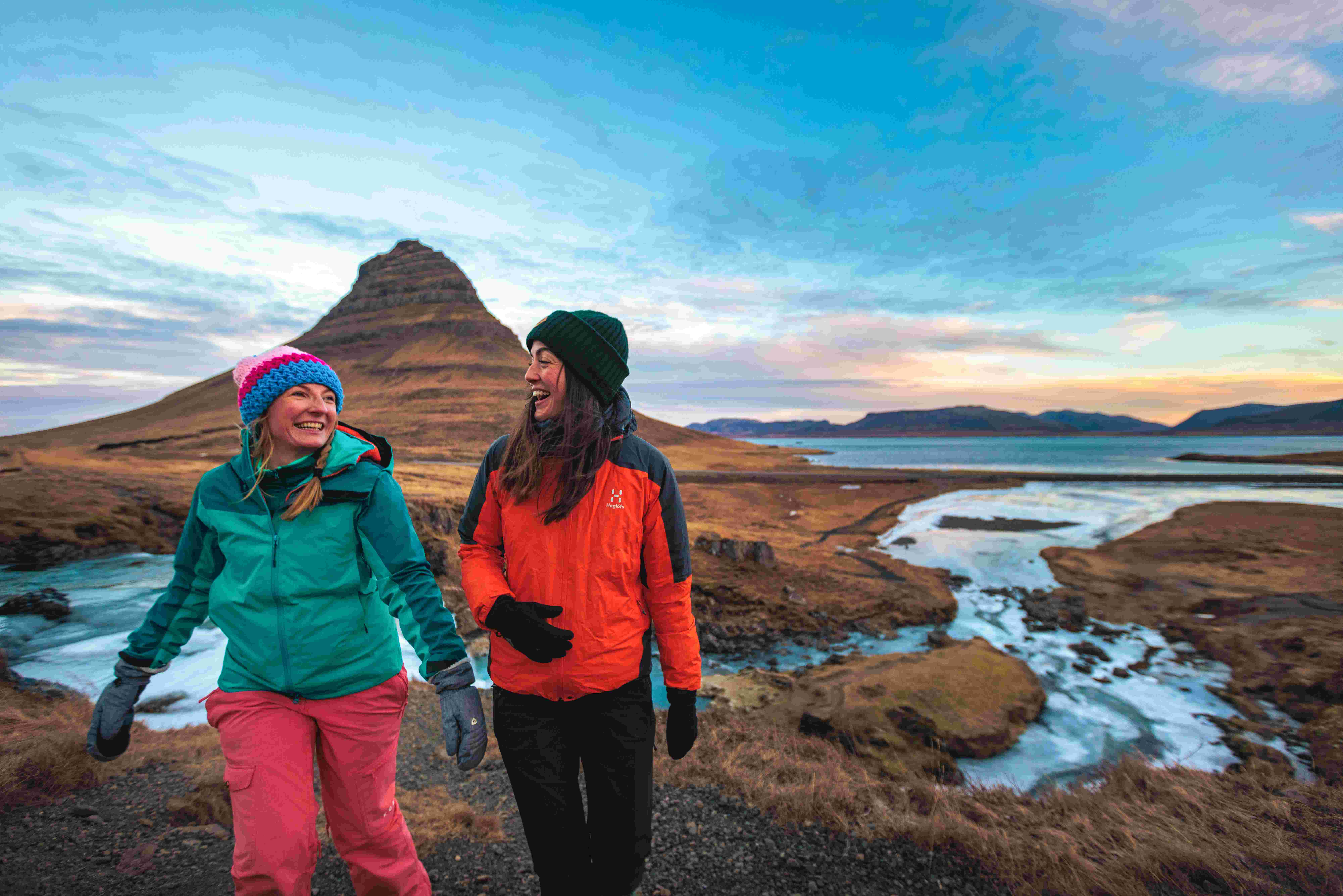 Two women laughing and smiling while wearing snow gear, in the middle of an empty dirt valley