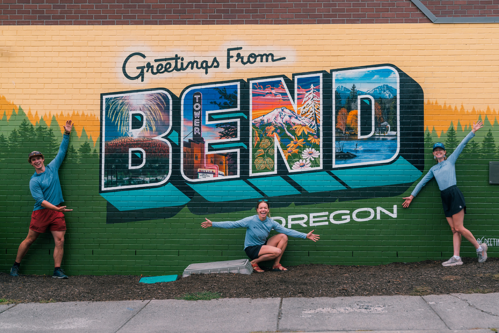 One man and two women in front of a colorful sign of Bend, Oregon