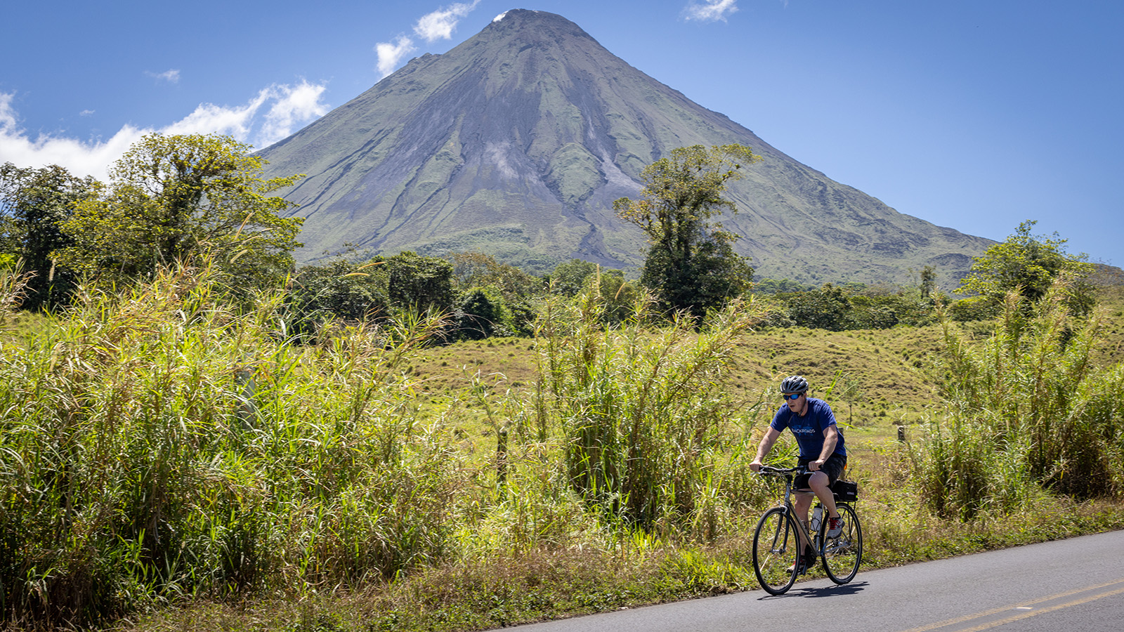 Biker on a road with a mountain and grassy field in the background