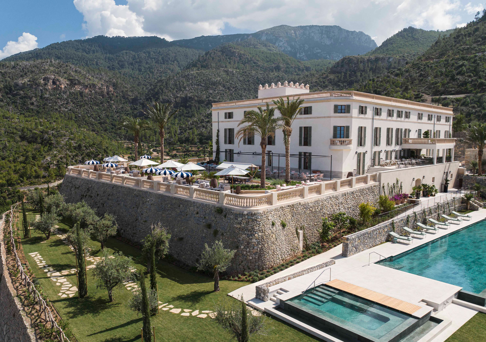 Long, white rectangular building with an outdoor pool on the right and large mountains in the background