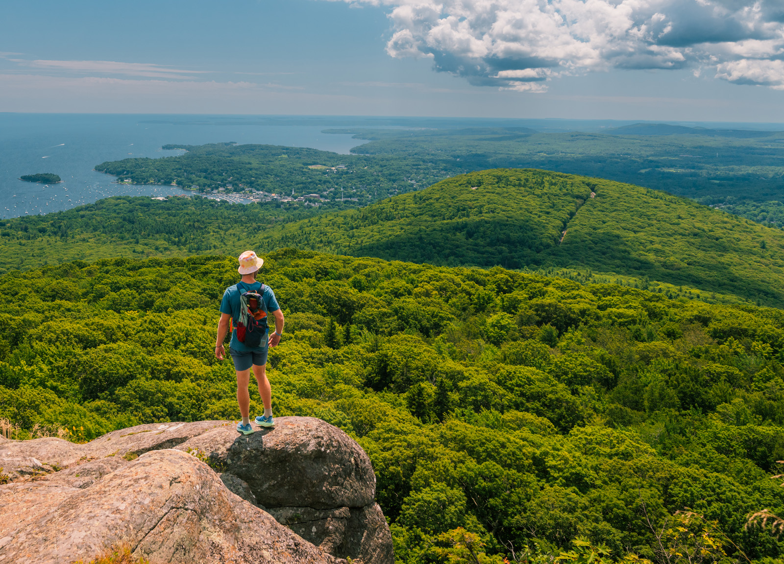 Man standing on the edge of a cliff, looking out towards a jungle