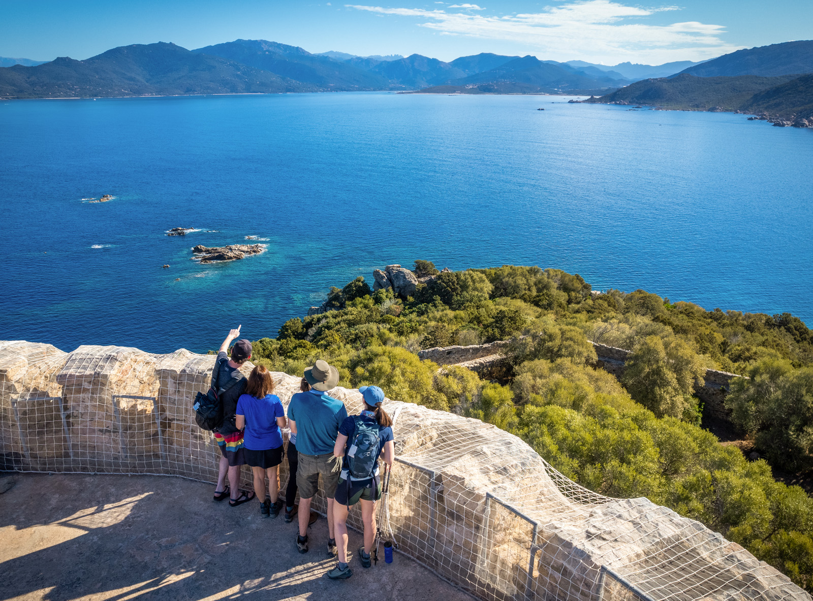 Group of men and woman on a tall rock path, overlooking to a large lake