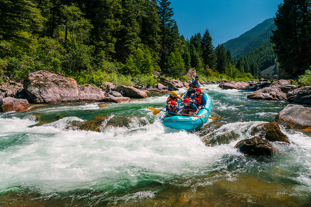 Group of people on a blue raft, paddling through an active river