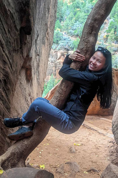 Woman smiling while hugging and hanging onto a tree