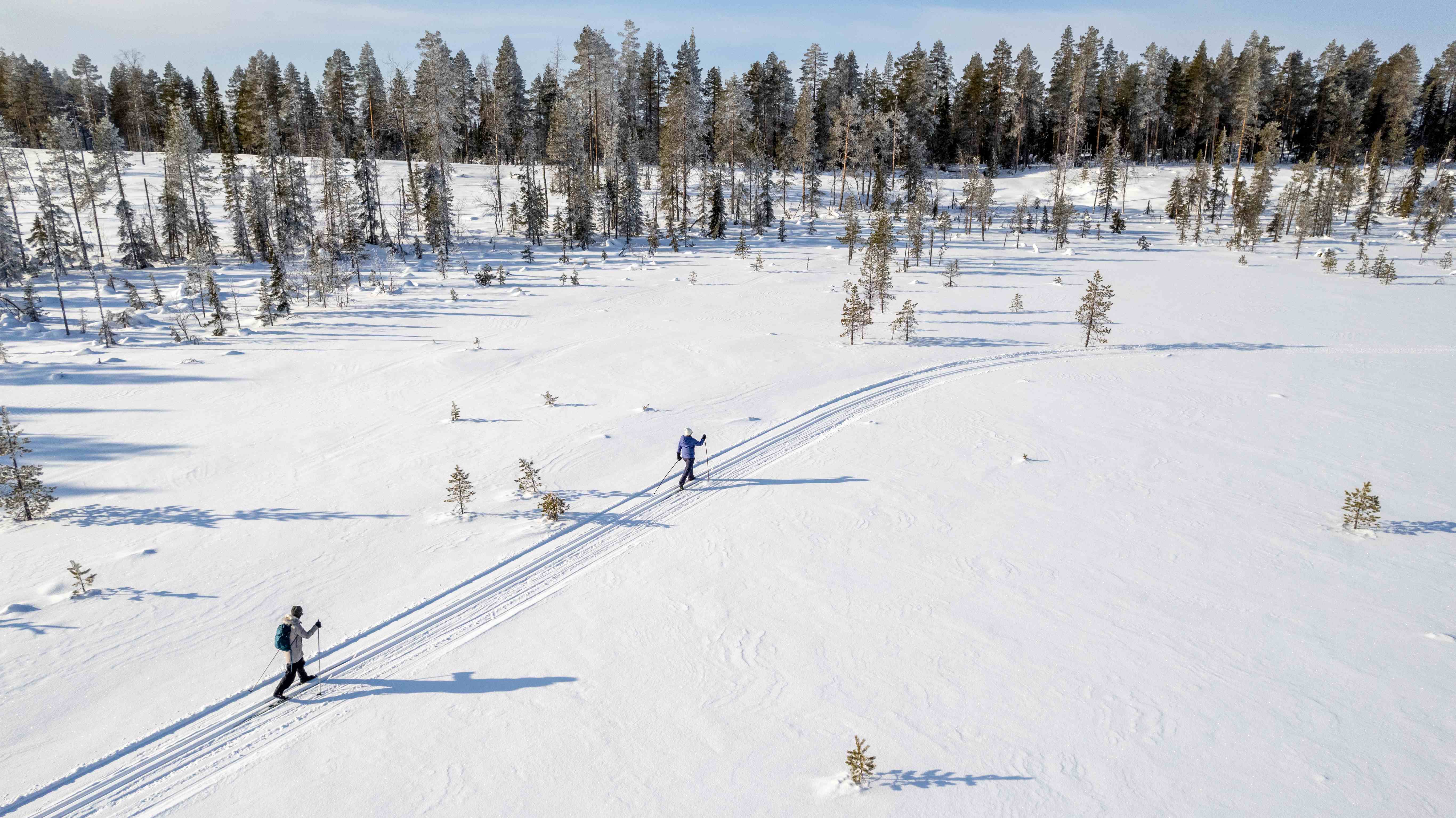 Two people with walking poles trekking through a valley of snow