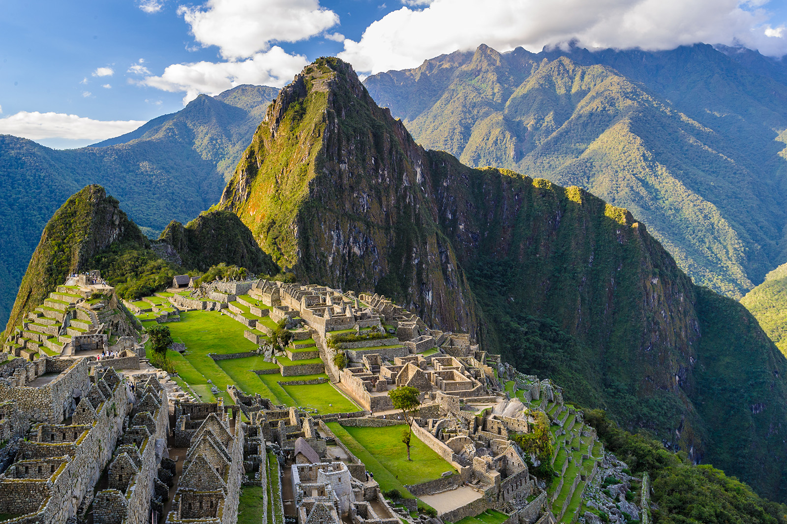 Historic ruins on top of a grassy hill, with tall, jagged mountains next to them