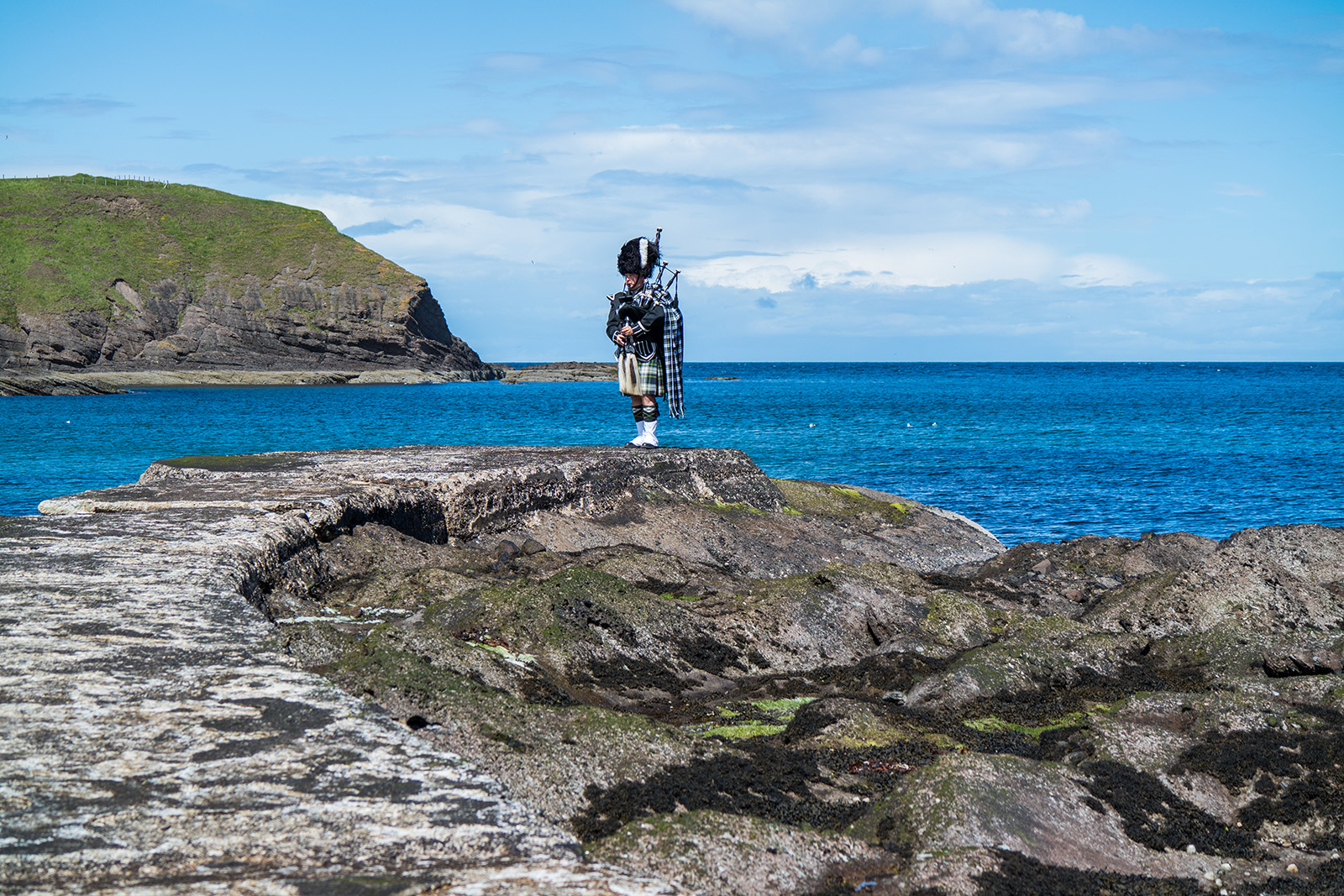 Man standing on rocks by the ocean playing the bagpipes