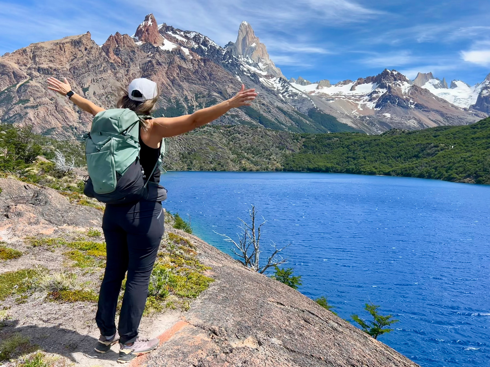 A person holds their arms wide open to a blue lake