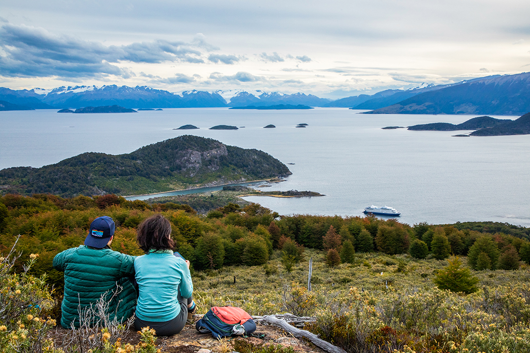 Man and woman sitting on a cliff overlooking the ocean