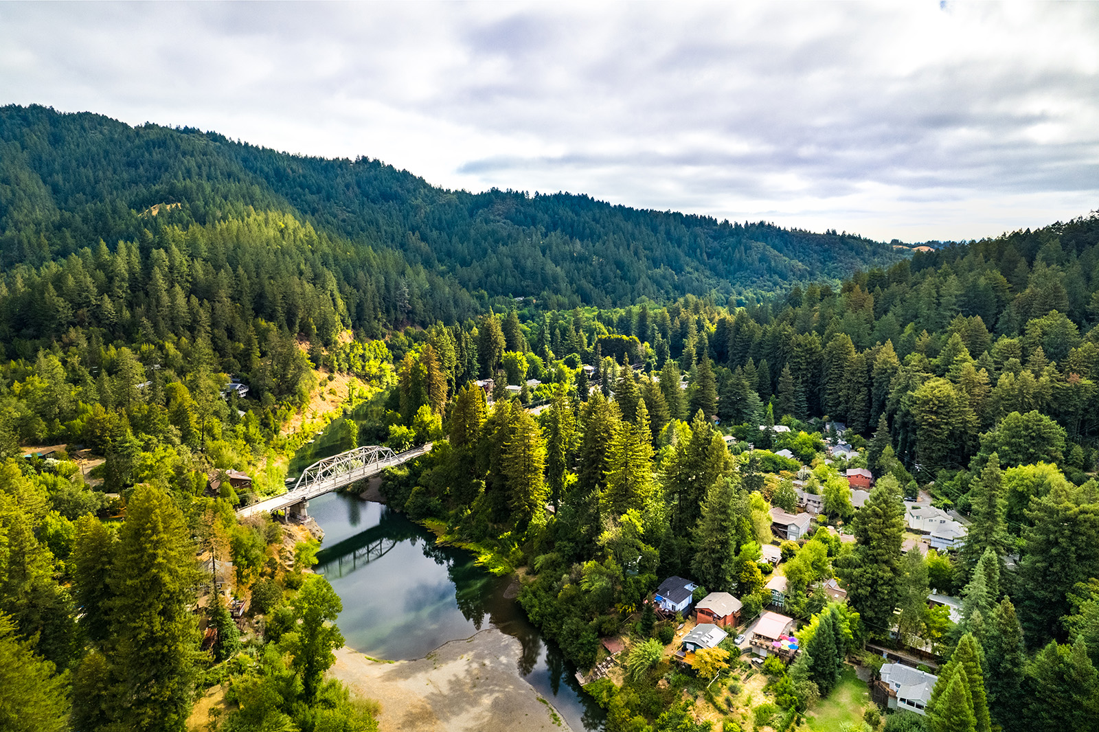 Small town surrounded by tall trees with a bridge over a river