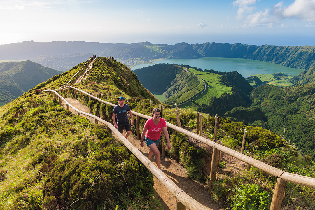 Man and woman walking along a dirt path with large, wooden handrails