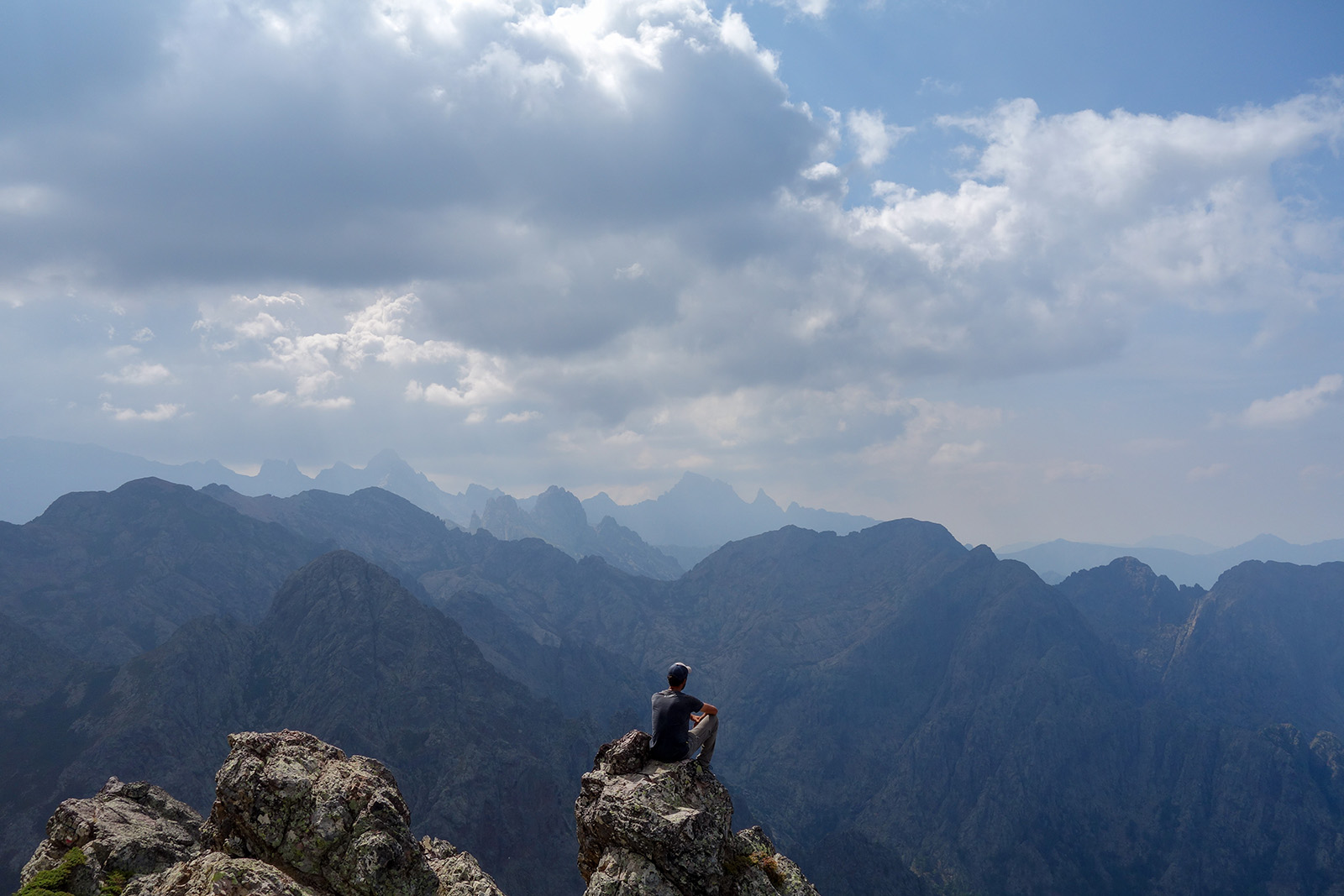 Man sitting on a cliff looking out to an open view of mountains