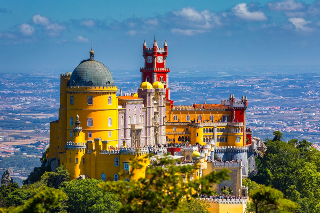 Yellow and red Spanish-style castle building with people standing on the outdoor patio
