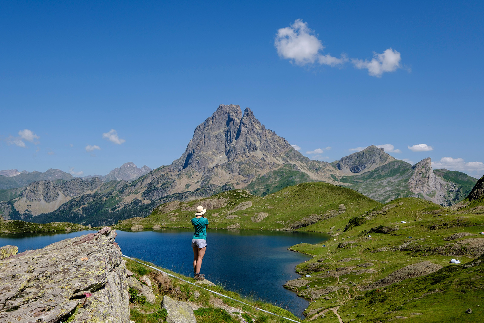 Woman standing on a cliff by a lake, looking out to a tall mountain
