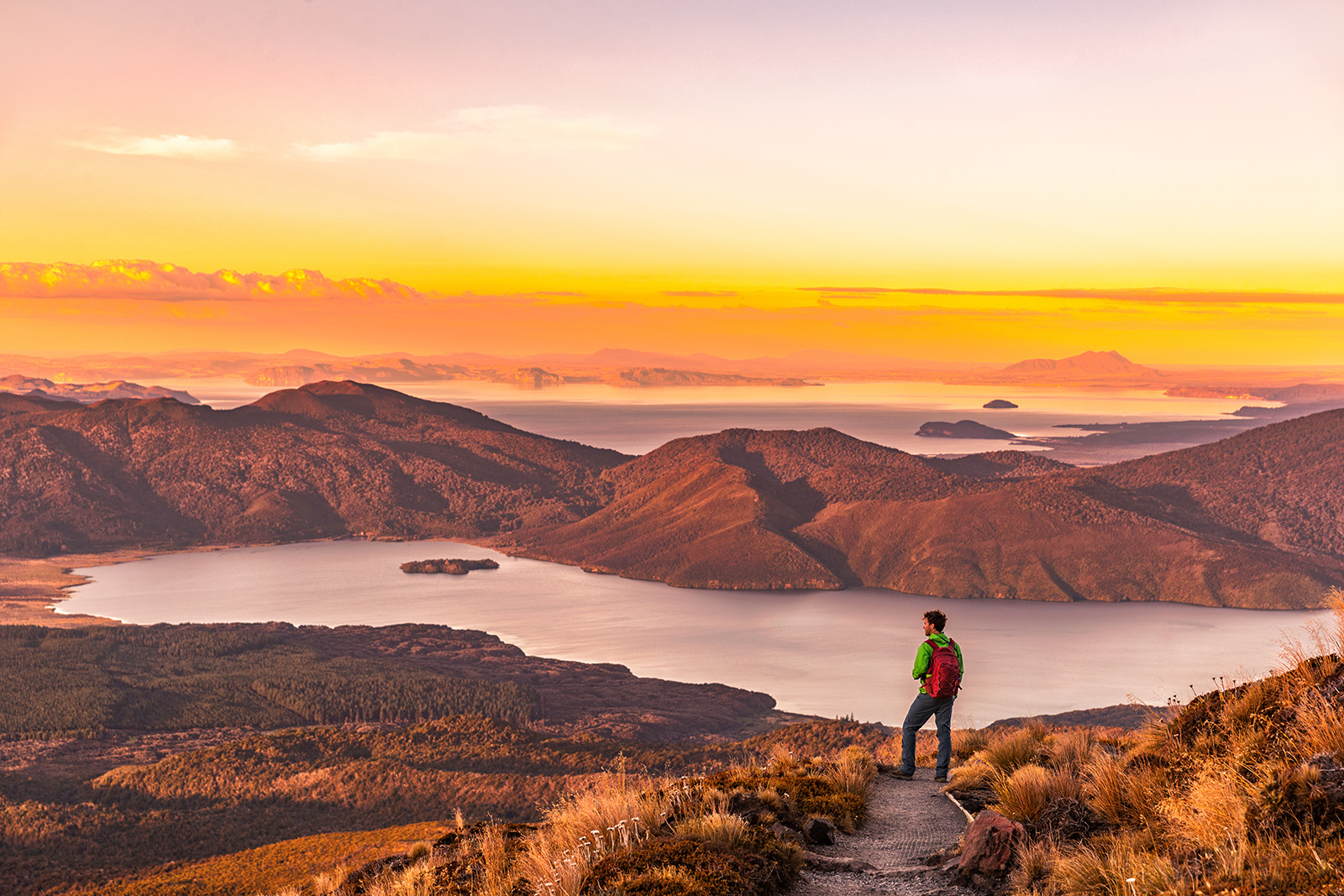 Man standing on a cliff with mountains and a river in the distance