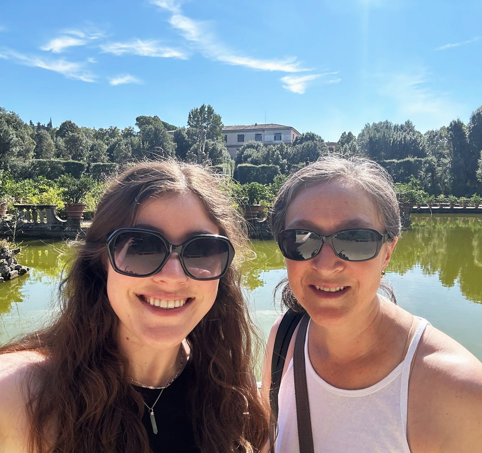 Two women wearing sunglasses, smiling while standing in front of a lake