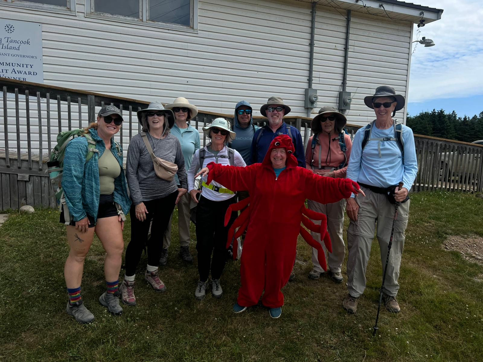Group of hikers in front of a building, smiling around someone wearing a lobster suit