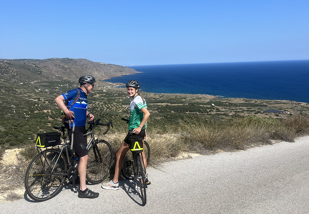 Man and woman turning around and smiling, while standing on their bikes on top of a hill