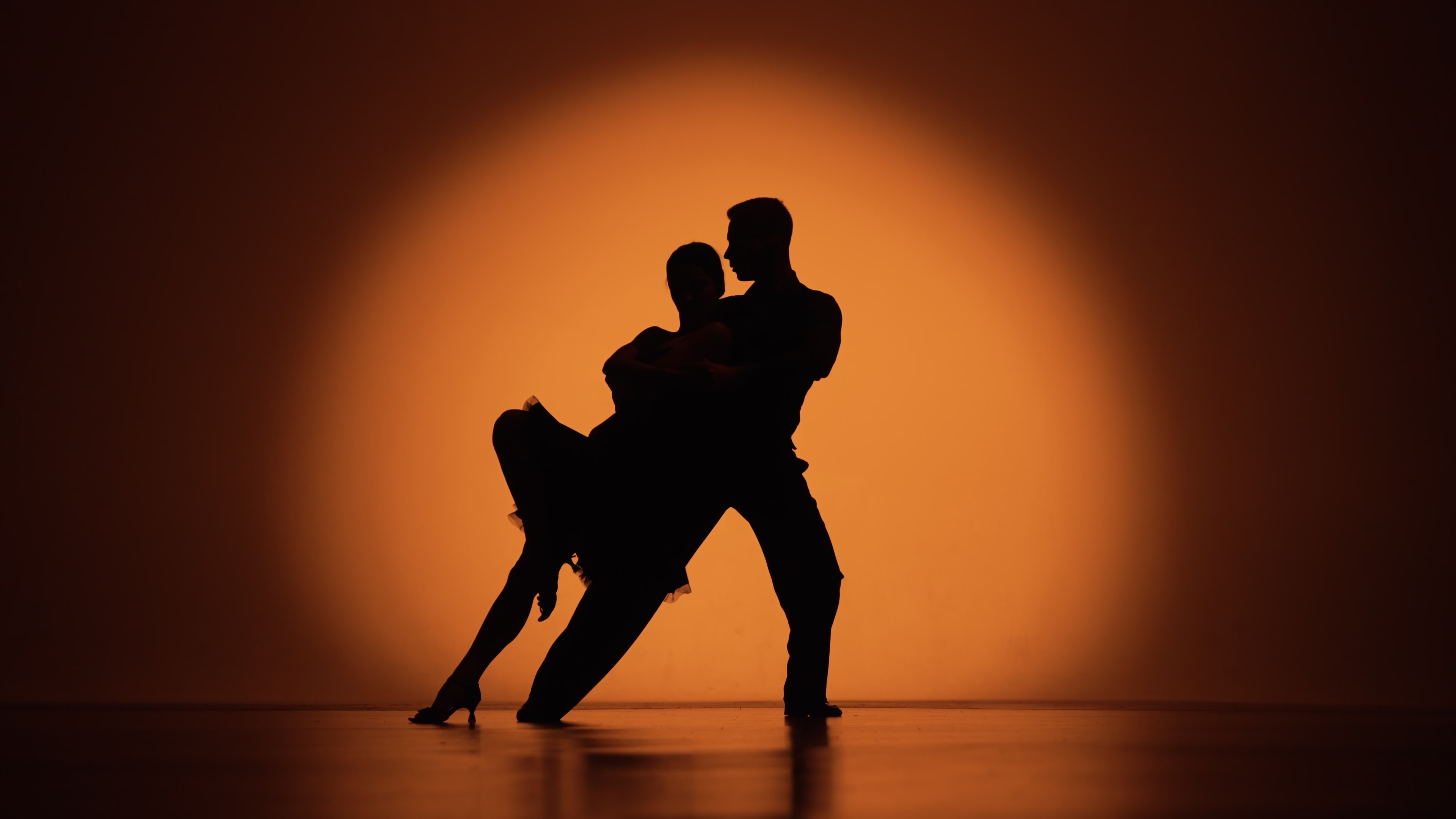 Silhouette of man and woman dancing in front of an orange wall