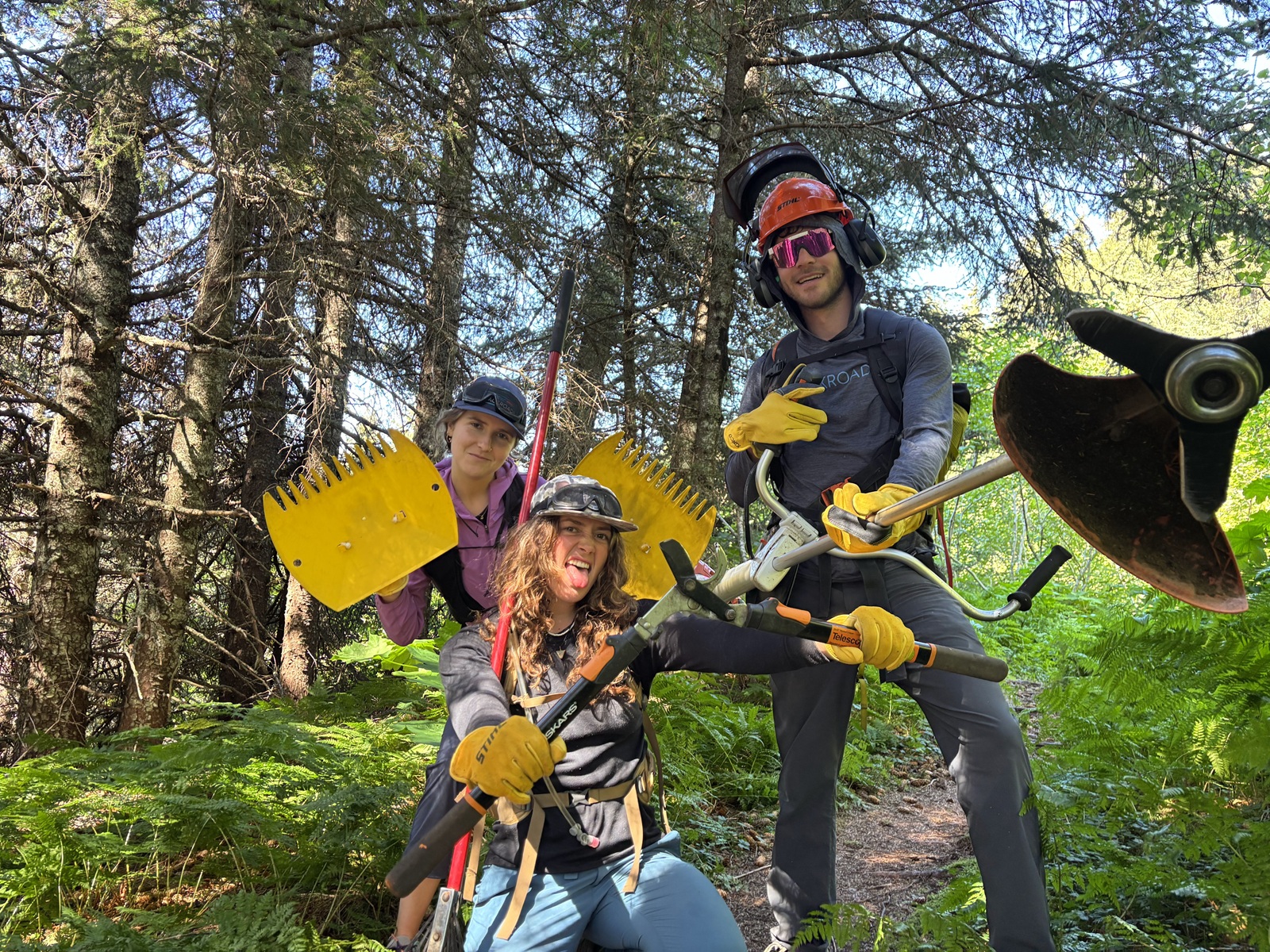 Two women and one man with gardening tools and goggles in the middle of a forest