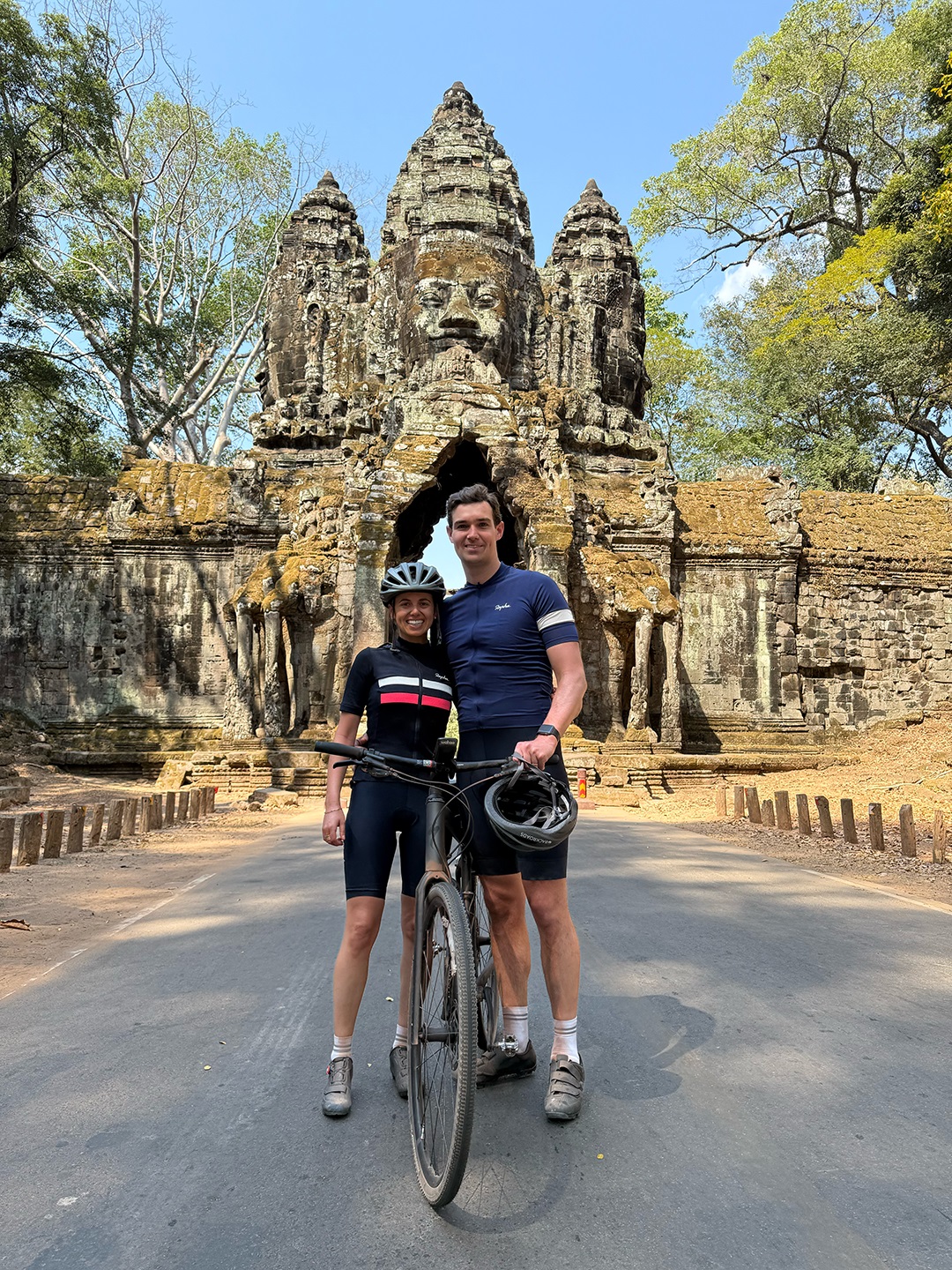 Man and woman smiling with a bike in between them, and ruins in the background
