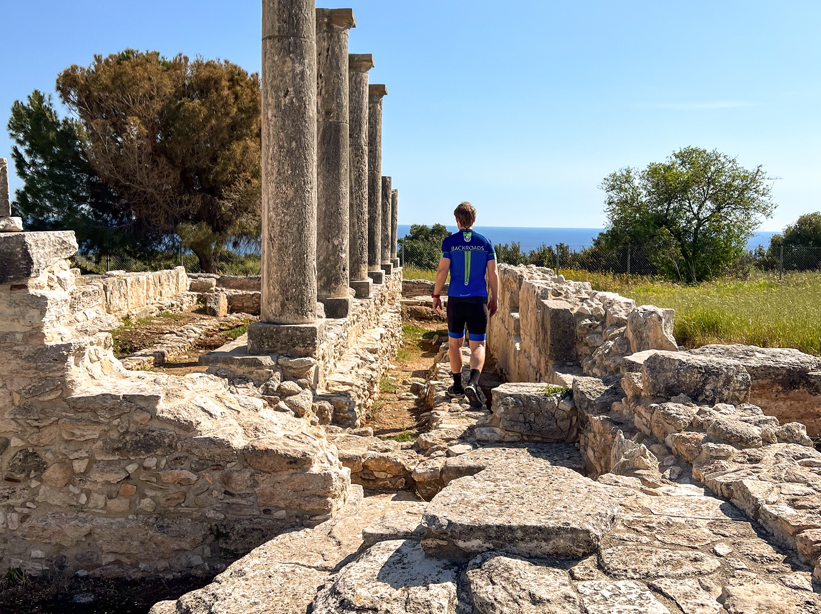 Man walking through temple ruins, with views of the ocean in the distance