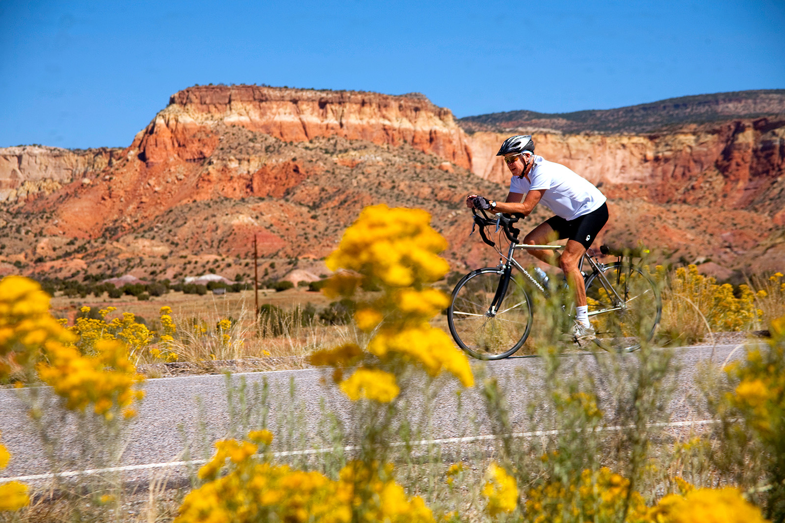 Man riding a bike on a road with orange canyons in the background